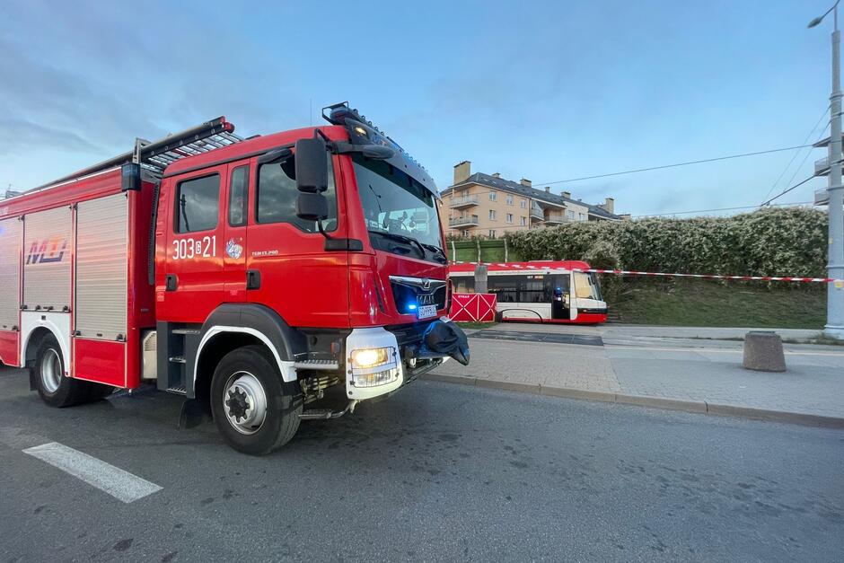 Na pierwszym planie samochód strażacki, w głębi zdjęcia - tramwaj. Oba pojazdy stoją w miejscu