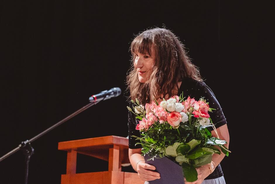 Kobieta w suknie z bukietem kwiatów stoi na scenie przed mikrofonem