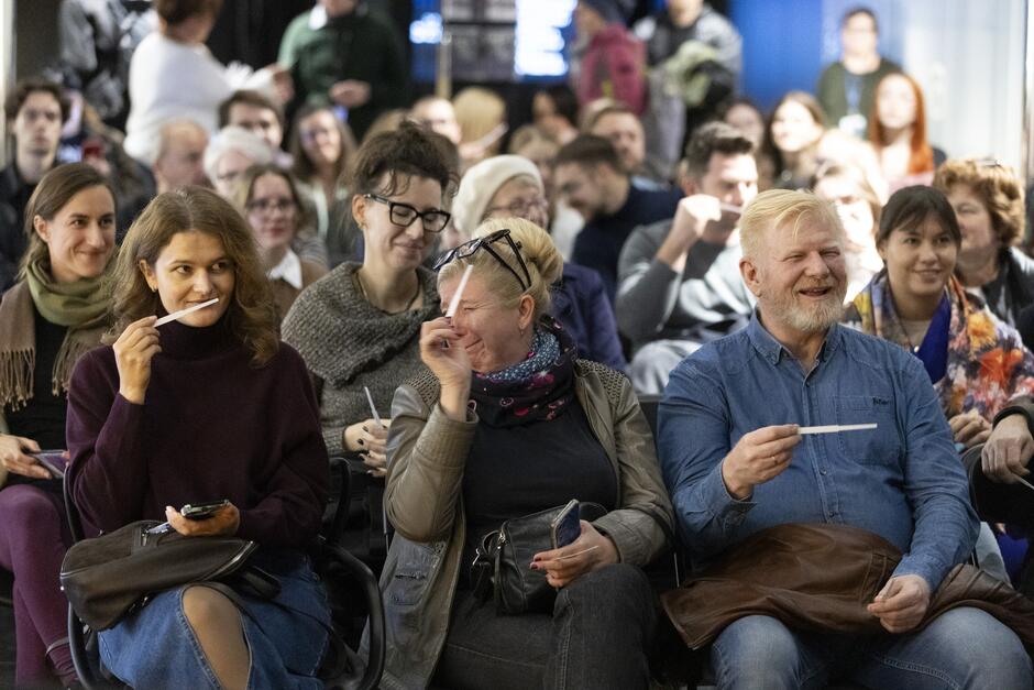 na zdjęciu kilkadziesiąt osób siedzi na krzesłach, w kilku rzędach, niektórzy wąchają naperfumowane białe paski papieru