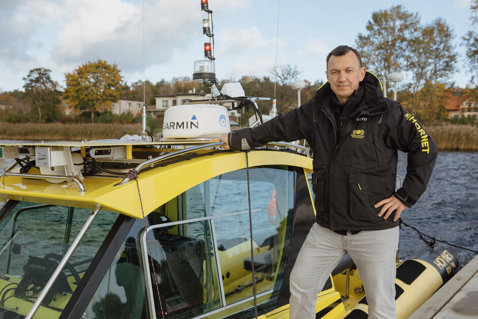 Na zdjęciu znajduje się mężczyzna stojący na łodzi o nazwie HORNET , ubrany w ciemną kurtkę z logo, wskazującą na profesjonalny charakter jego pracy. 