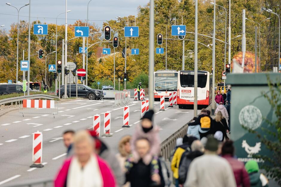 na zdjęciu ulica wygrodzona słupkami biało czerwonymi, ulica jedzie autobus miejski, po prawej widać na chodniku kilka idących osób