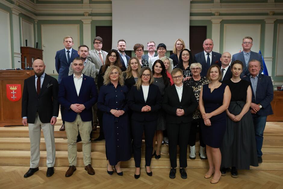 na zdjęciu pozuje około dwudziestu osób, stoją w trzech rzędach na schodkach, wszyscy w odświętnych strojach