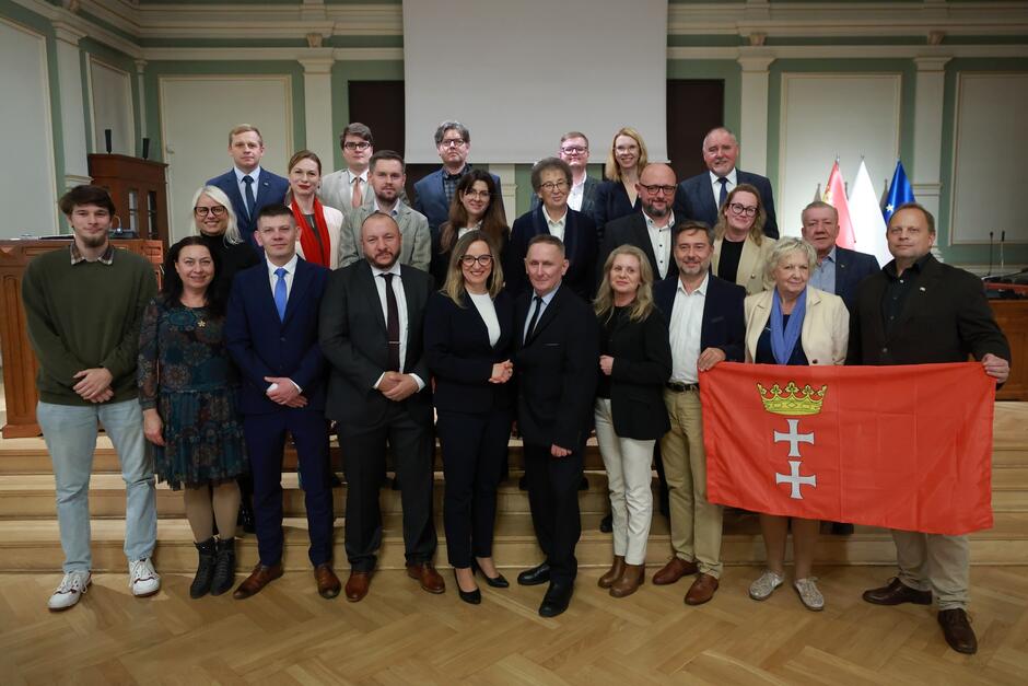 na zdjęciu pozuje około dwudziestu osób, stoją w trzech rzędach na schodkach, wszyscy w odświętnych strojach