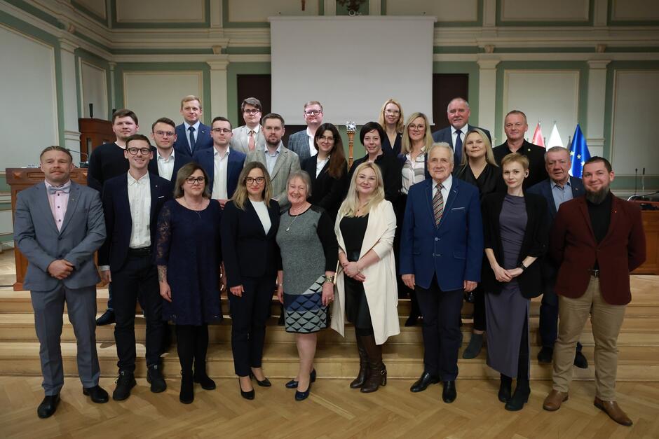 na zdjęciu pozuje około dwudziestu osób, stoją w trzech rzędach na schodkach, wszyscy w odświętnych strojach 