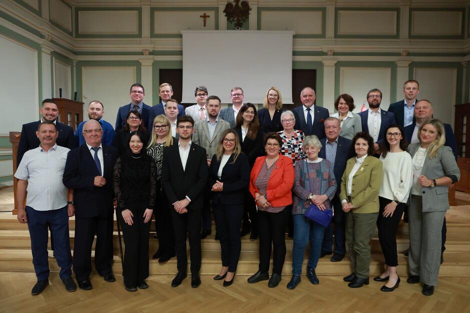 na zdjęciu pozuje około dwudziestu osób, stoją w trzech rzędach na schodkach, wszyscy w odświętnych strojach 