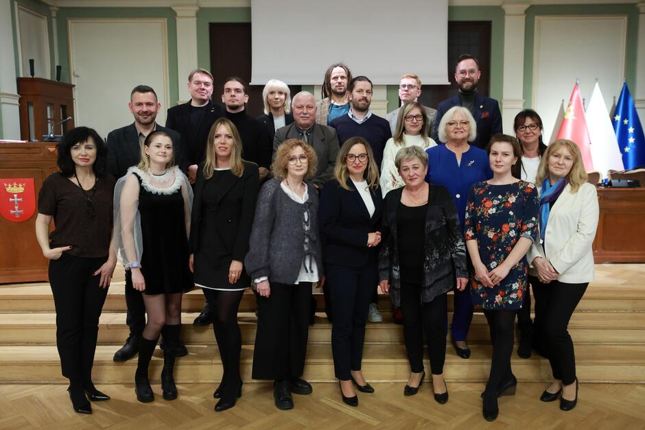 na zdjęciu pozuje około dwudziestu osób, stoją w trzech rzędach na schodkach, wszyscy w odświętnych strojach 