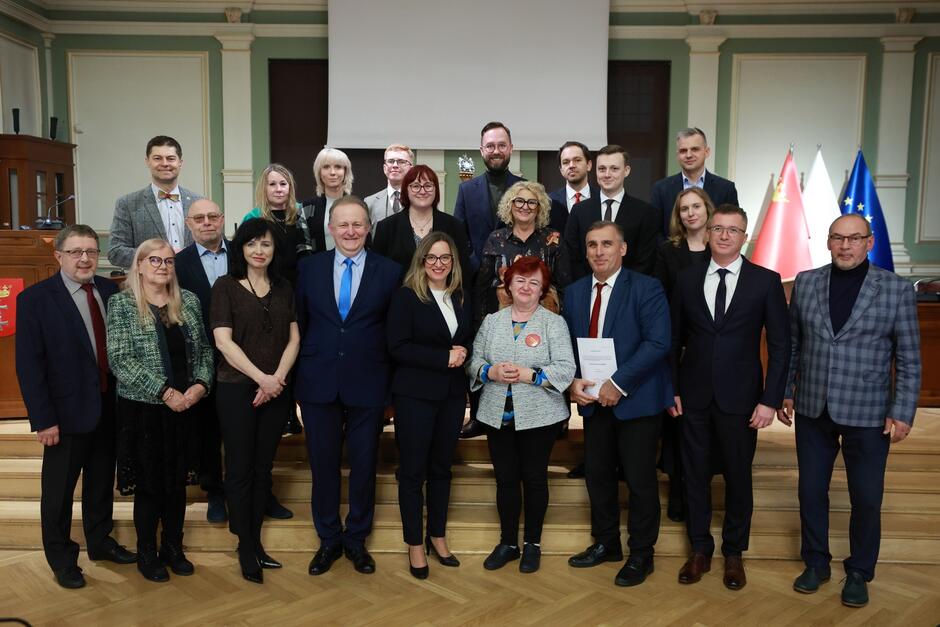 na zdjęciu pozuje około dwudziestu osób, stoją w trzech rzędach na schodkach, wszyscy w odświętnych strojach