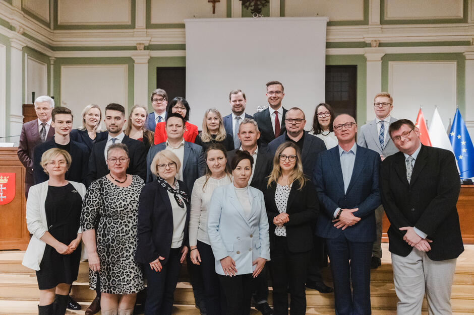 na zdjęciu grupa ponad dwudziestu osób, pozują do zdjęcia stojąc na schodach w trzech rzędach