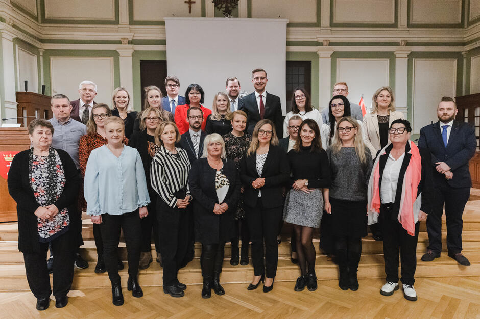 na zdjęciu grupa ponad dwudziestu osób, pozują do zdjęcia stojąc na schodach w trzech rzędach