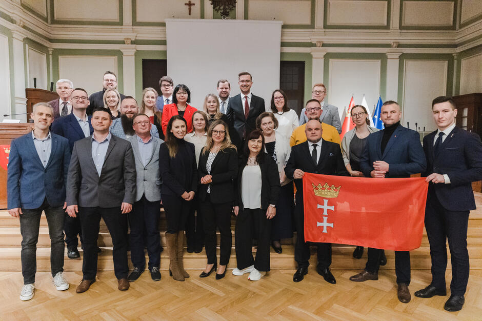 na zdjęciu grupa ponad dwudziestu osób, pozują do zdjęcia stojąc na schodach w trzech rzędach