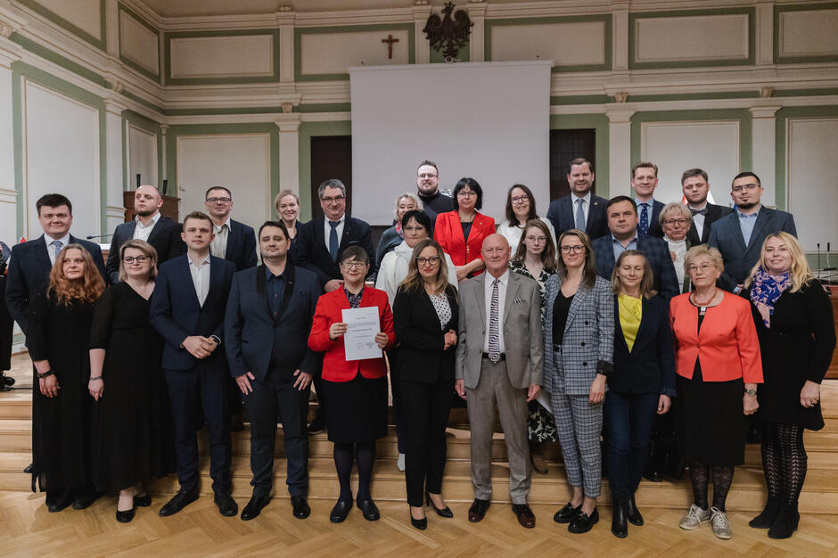 na zdjęciu grupa ponad dwudziestu osób, pozują do zdjęcia stojąc na schodach w trzech rzędach