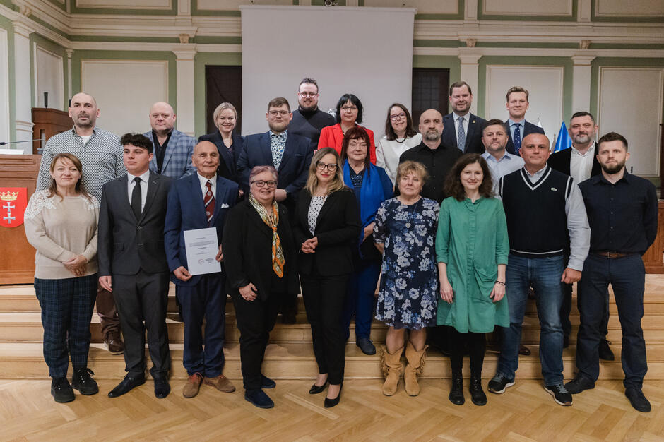 na zdjęciu grupa ponad dwudziestu osób, pozują do zdjęcia stojąc na schodach w trzech rzędach