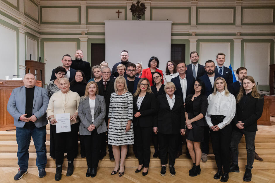 na zdjęciu grupa ponad dwudziestu osób, pozują do zdjęcia stojąc na schodach w trzech rzędach