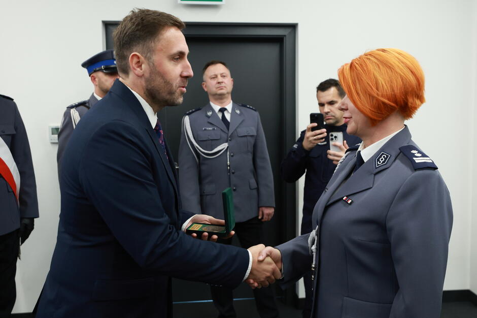 na zdjęciu po lewej mężczyzna w średnim wieku w garniturze, wiceprezydent gdańska wręcza medal policjantce, trzyma ją za rękę, policjantka na rudy kolor włosów