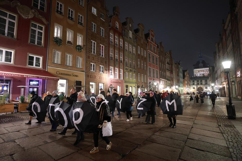 Ulica miasta idą wieczorem ludzie i niosą rozłożone parasole, które tworzą napis stop faszyzm .