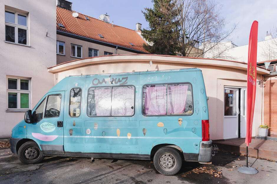 niebieski samochód - bus ozdobiony wawałkami owcu - arbuza, w tle niski budynek i czerwona flaga z napisem Gdańsk