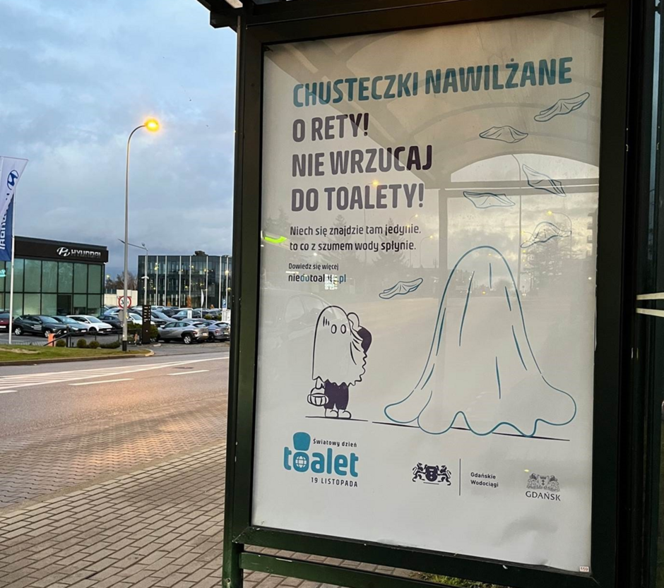 Na zdjęciu znajduje się reklama umieszczona w wiacie przystankowej, zachęcająca do niewrzucania nawilżanych chusteczek do toalety. Plakat utrzymany w humorystycznym tonie, wspierany przez Gdańskie Wodociągi, promuje odpowiedzialne korzystanie z toalety w ramach Światowego Dnia Toalet 19 listopada.