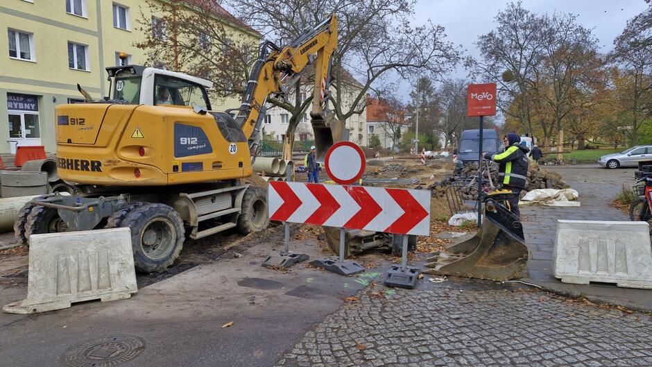 na zdjęciu remontowana ulica, na pierwszym planie, po lewej stoi duża żółta koparka, obok znaku drogowego w biało czerwone pasy