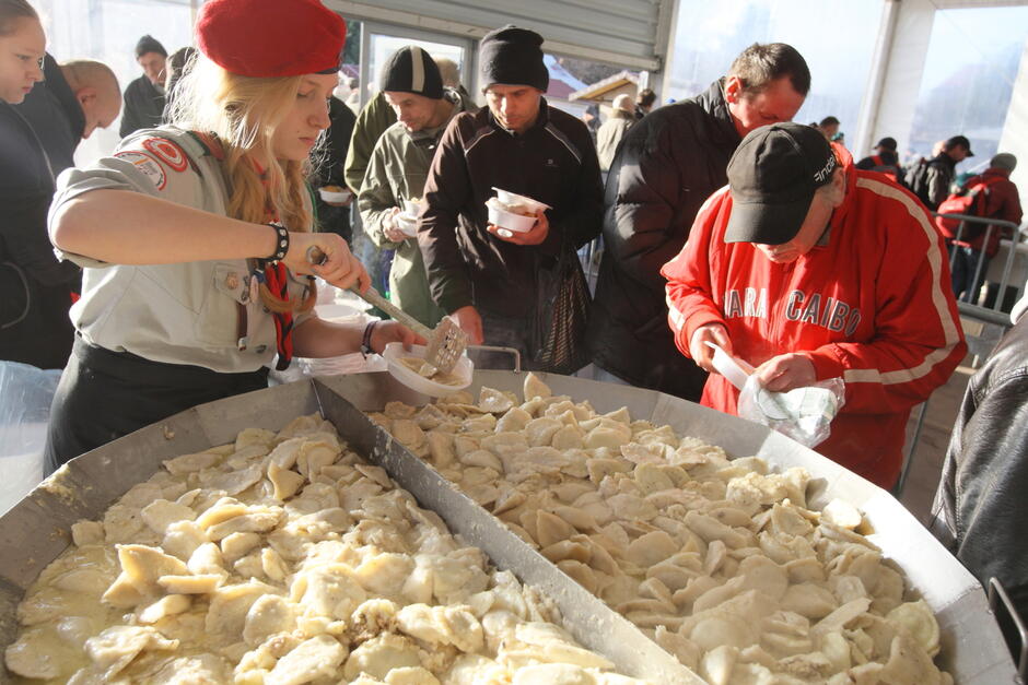 wielki talerz z pierogami, około 100 sztuk pierogów, harcerki nakładają pierogi do miseczek, w tle kolejka ludzi 