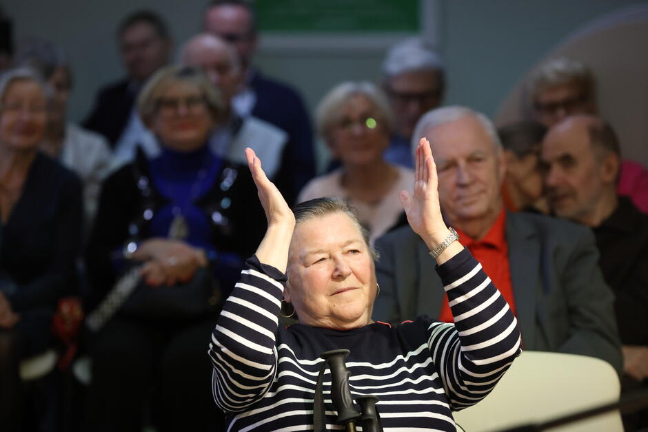 Grupa osób siedzących na krzesłach podczas uroczystości. Biją brawo