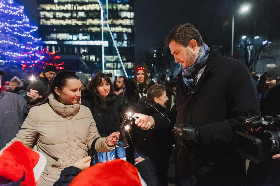 grupka ludzi rozpala zimne ognie, kobieta i mężczyzna na pierwszym planie