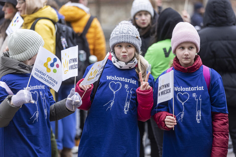 na zdjęciu trzy dziewczynki, w zimowej odzieży, mają koszulki z napisem wolontariat