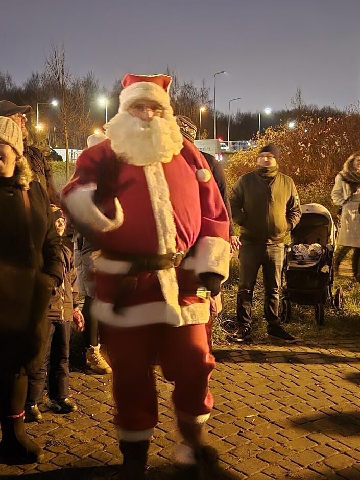 Mikołaj w czerwonym stroju z brodą, w tle grupa ludzi