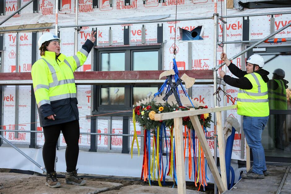 na zdjęciu dwóch budowlańców w roboczych strojach, trzymają wiechę na linie