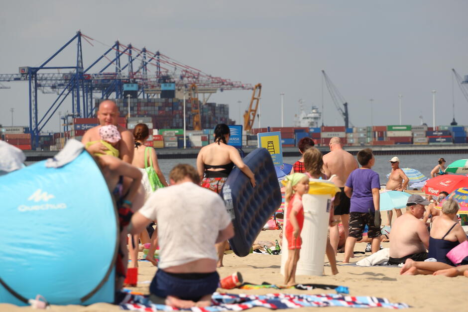 plaża, duża grupa ludzi, w tle dźwigi portowe