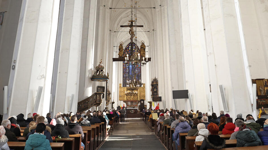 Wnętrze kościoła, w ławach siedzą ludzie. W tle ołtarz