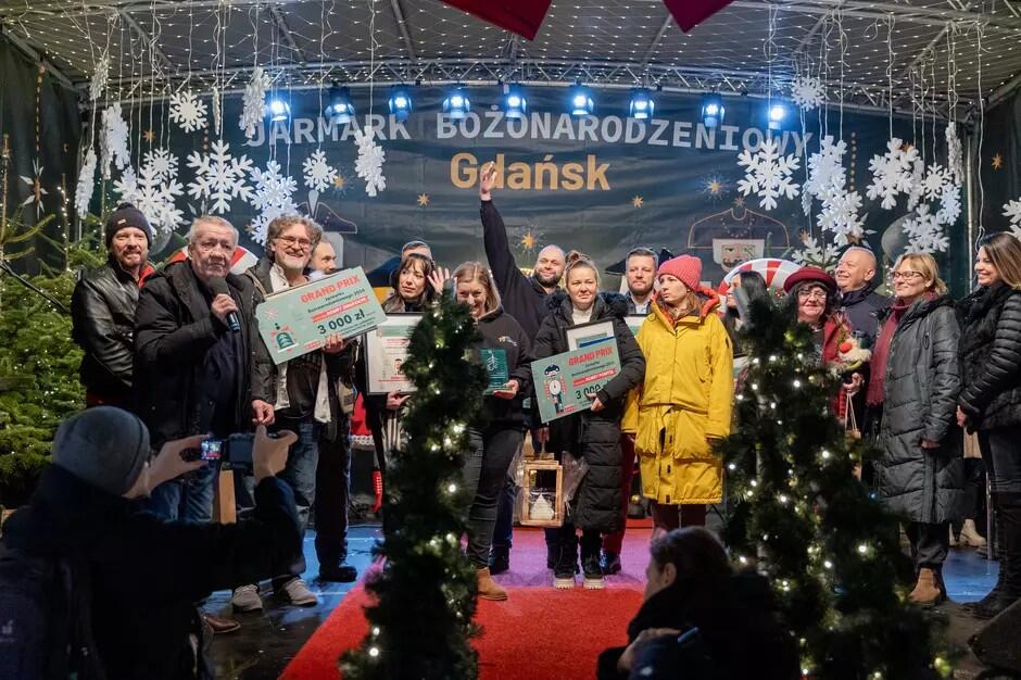 Kilkanaście osób stoi na scenie usytuowanej na świeżym powietrzu, niektórzy trzymają w dłoniach dyplomy