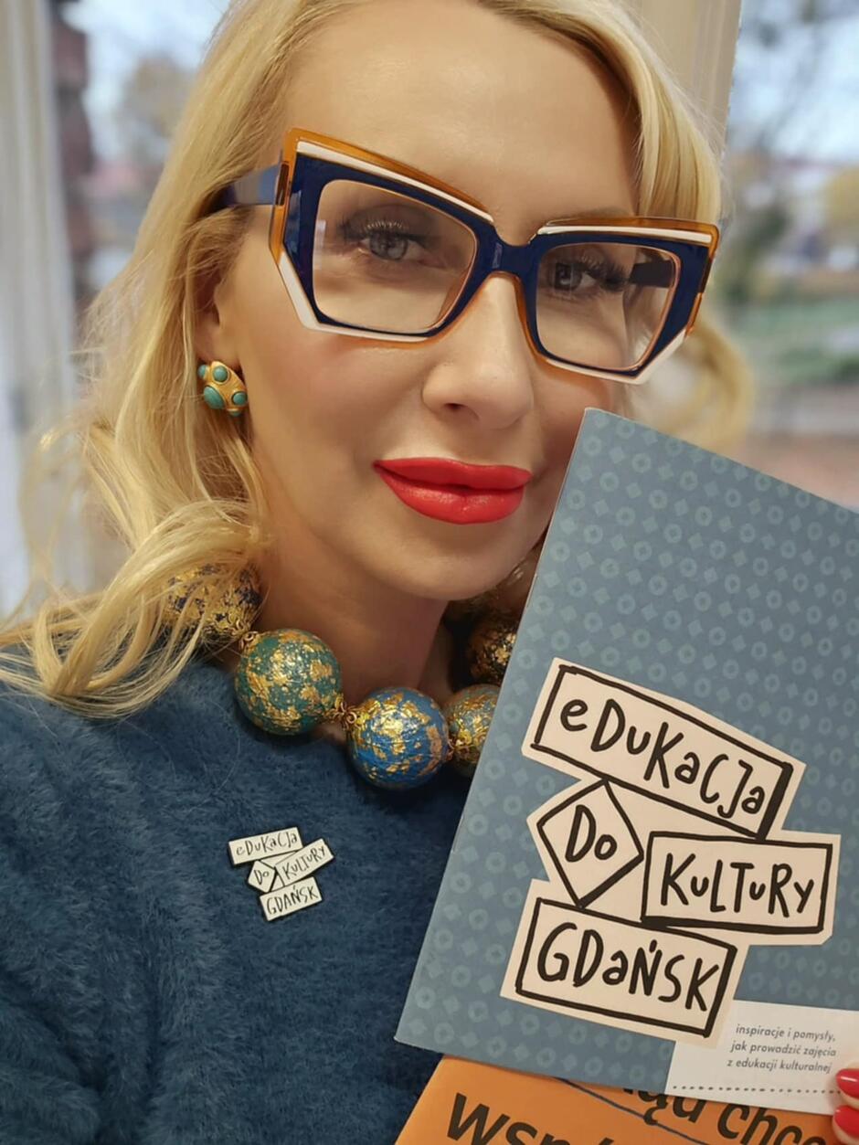 Blondynka, kobieta prezentuje książkę o tytule edukacja do kultury 