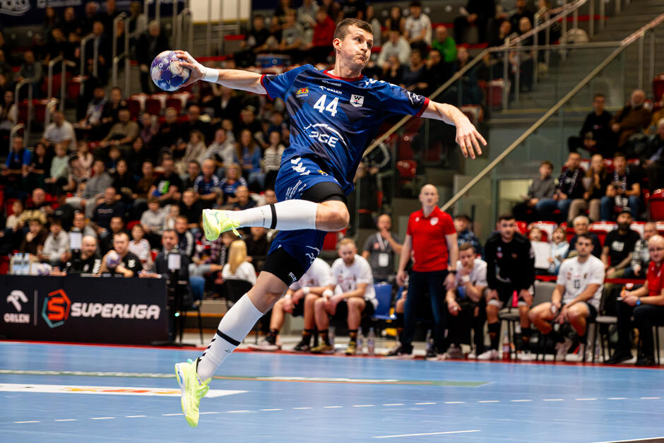 Mężczyzna w niebieskim stroju z piłką w prawej ręce przygotowaną do rzutu