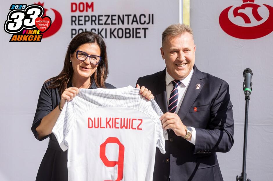 Kobieta po lewej, po prawej mężczyzna, który wręcza biało-czerwoną koszulkę