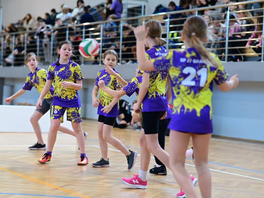 Dziewczynki w strojach sportowych na sali, w stronę jednej z nich leci piłka 