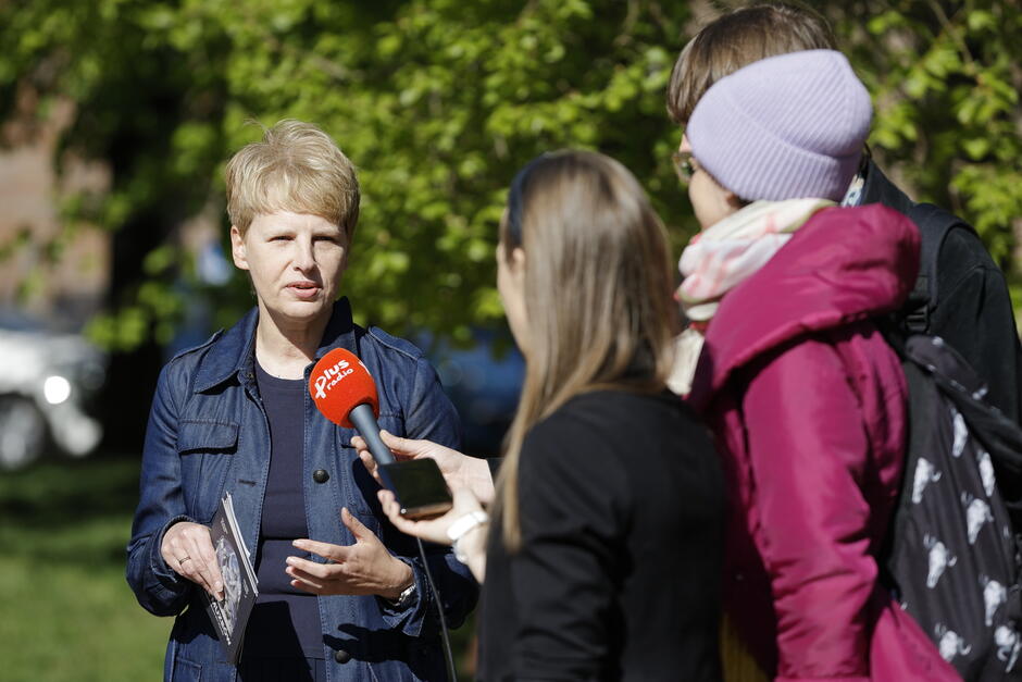 Kobieta mówi do mikrofonu, wokół niej stoją dziennikarze.