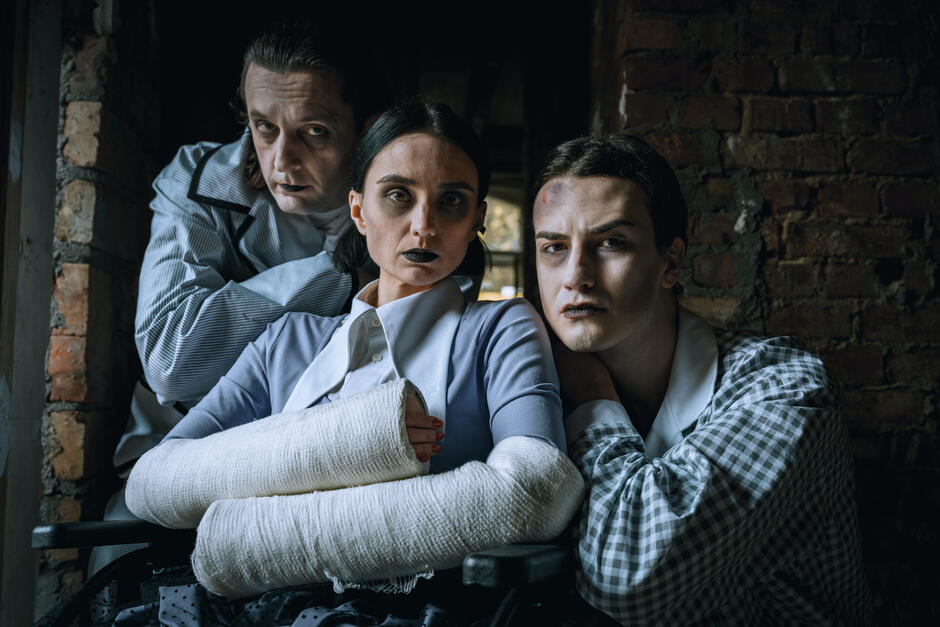Troje aktorów około 20. roku życia scharakteryzowanych na pacjentów szpitala w stylu halloween