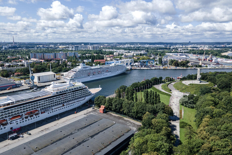 To zdjęcie z lotu ptaka przedstawia port w Gdańsku oraz jego okolicę, a na pierwszym planie widoczne są dwa luksusowe statki wycieczkowe zacumowane przy nabrzeżu. Obraz ukazuje nie tylko żeglugową infrastrukturę, ale również turystyczny i historyczny charakter tego miejsca.