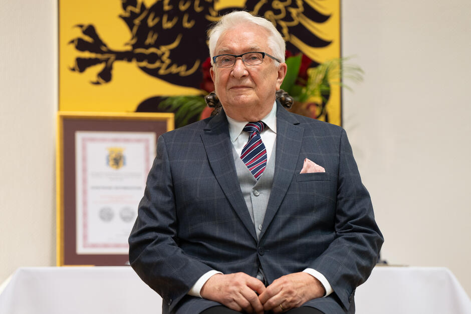 Starszy siwy mężczyzna w garniturze siedzi na krześle