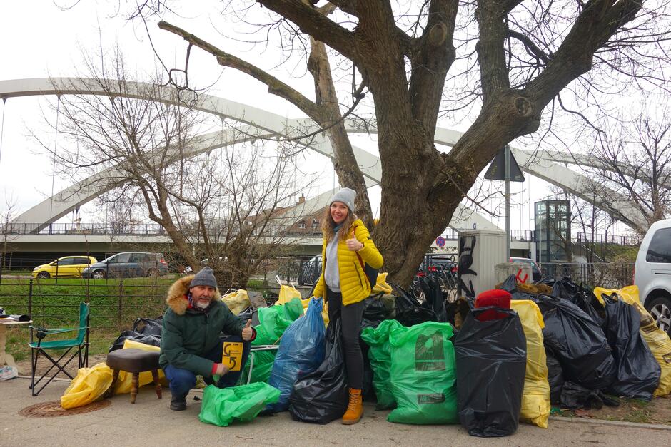 Dwoje wolontariuszy pod drzewem wśród masy plastikowych worków wypełnionych śmieciami