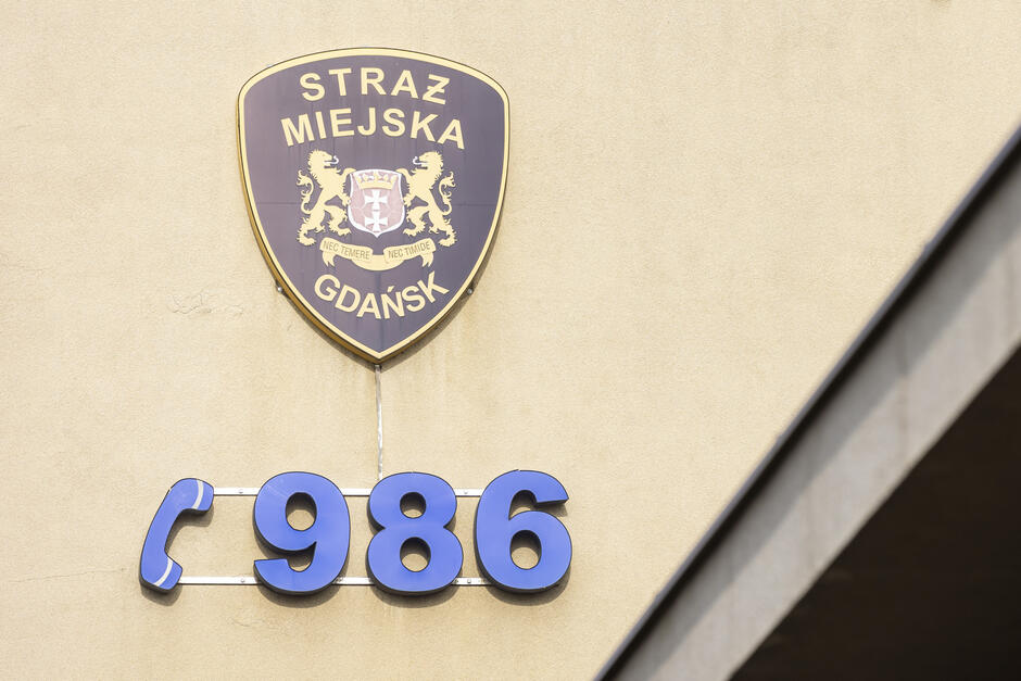 Ściana komisariatu Straży Miejskiej z godłem Gdańska oraz numerem telefonu 986.