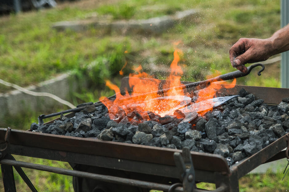 Na grillu żarzą się węgle, widać rękę, która rusza je pogrzebaczem.