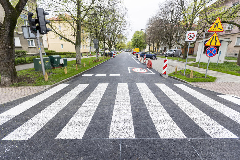 na zdjęciu wyremontowana ulica z wymalowanym przejściem dla pieszych w tle drzewa, trawniki, oznakowanie drogowe