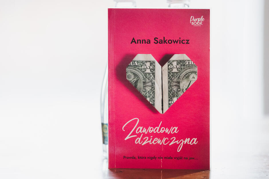 Na okładce książki „Zawodowa dziewczyna” Anny Sakowicz widnieje origami w kształcie serca wykonane z dolarowego banknotu, umieszczone na intensywnie różowym tle. Pod tytułem znajduje się intrygujące hasło: „Prawda, która nigdy nie miała wyjść na jaw…”