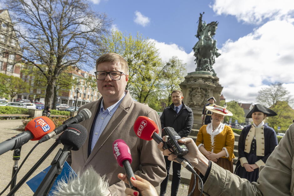 Mężczyzna lat około 35 przemawia do mikrofonów