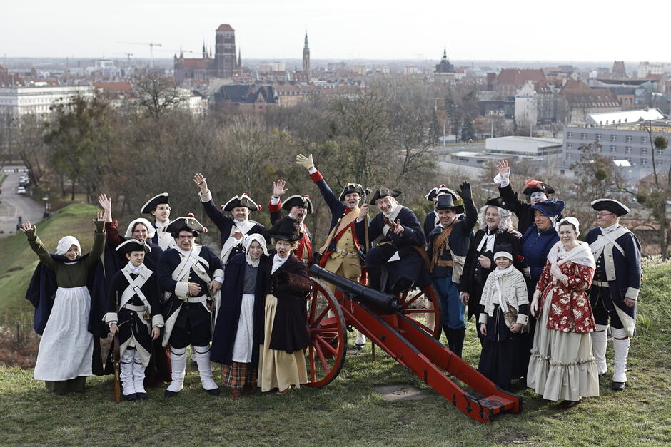 Inscenizatorzy w mundurach i strojach z epoki pozują do zdjęcia na górze nad miastem.