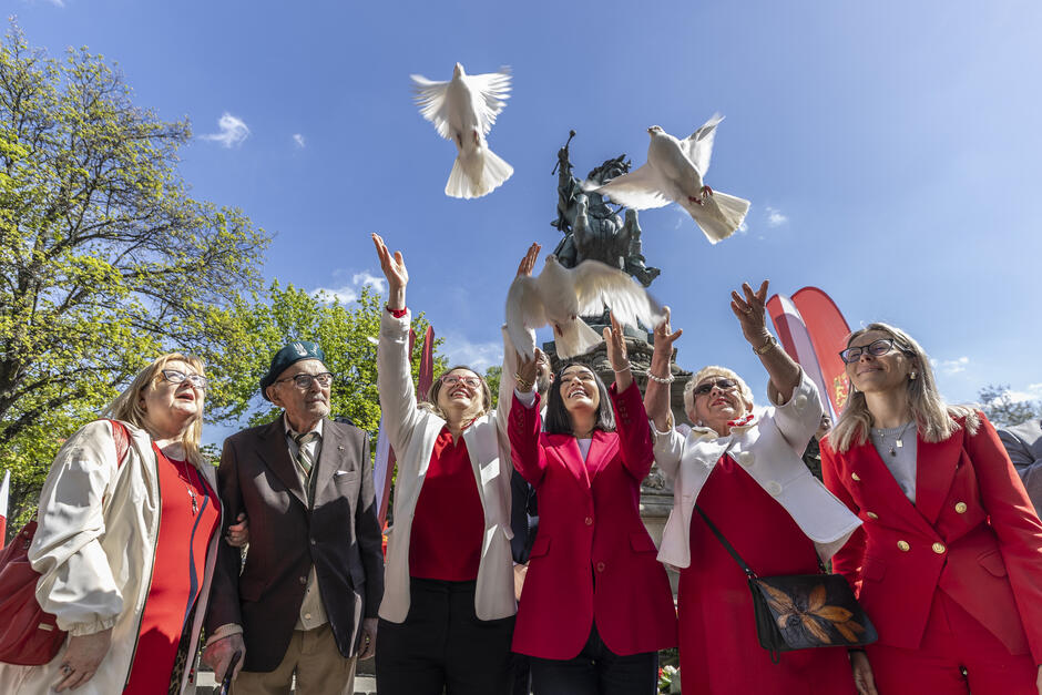 Kilka osób stoi obok siebie, trzy z nich wypuszczają w powietrze gołębie