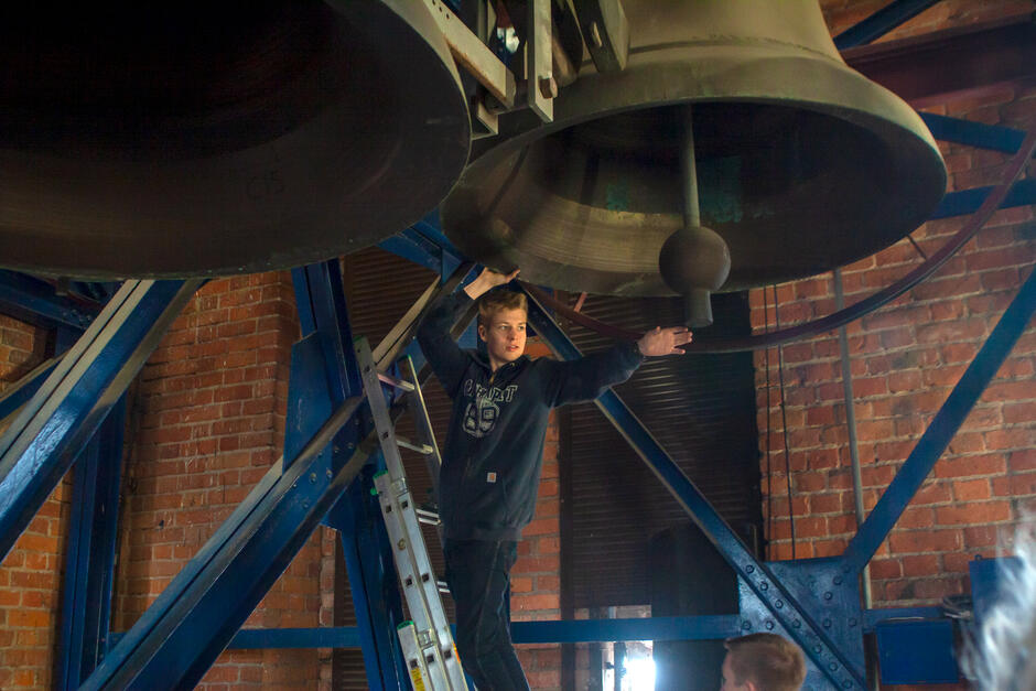 Młody mężczyzna wychyla się spod dolnej krawędzi dzwonu, by dotknąć jego serca