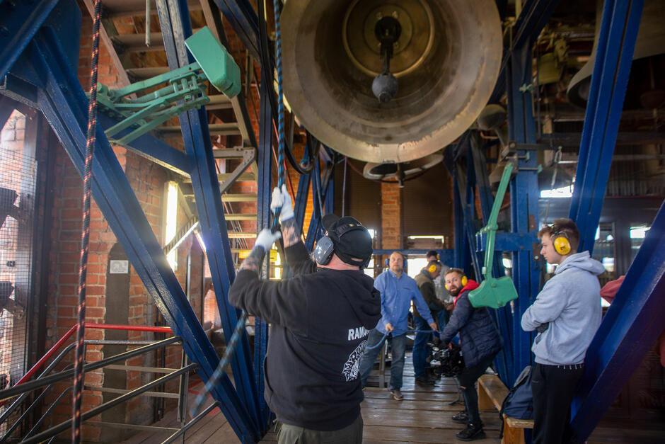 Kilka osób w wysokim pomieszczeniu, ciągną sznury od dzwonów