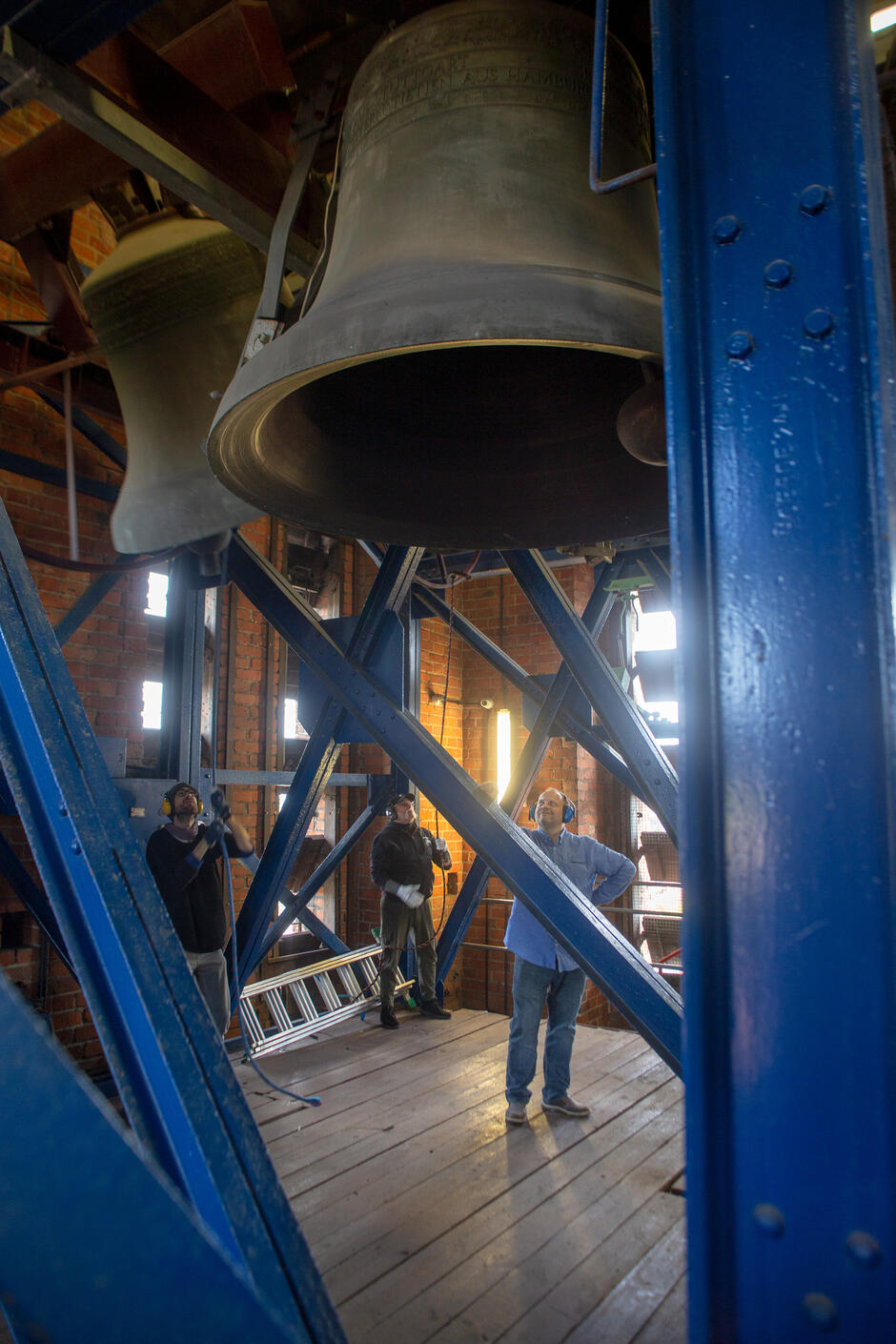 Wysokie zdjęcie w pionie, mężczyzna stoi pod wielkim dzwonem, wiszącym w wieży